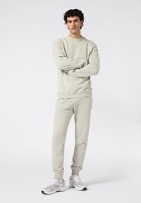 Conjunto de chándal gris claro que incluye una sudadera de cuello redondo y pantalones ajustados. Textura suave, puños acanalados y un sutil logotipo en el pecho.