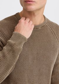 Brązowy sweter dzianinowy z fakturowanym wzorem, z prążkowanymi mankietami i dekoltem. Tkanina ma średnią wagę, a krój jest dopasowany z okrągłym dekoltem.