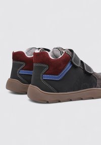 Zapatos negros y marrones con acentos de ante en burdeos y azul, que presentan una correa de velcro y una suela de goma texturizada.