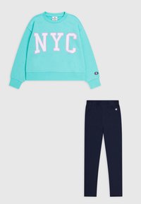 Felpa color turchese con la scritta "NYC" in bianco e rosa, abbinata a leggings blu scuri. Entrambi realizzati in tessuto morbido; la felpa ha polsini a coste.