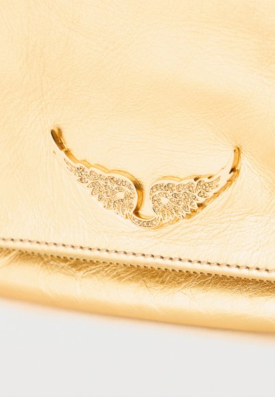 Επιφάνεια από χρυσό δέρμα με ένα μικρό, περίτεχνο, χρυσό έμβλημα σε σχήμα φτερού διακοσμημένο με μικρούς κρυστάλλους και λεπτομερείς οπές.