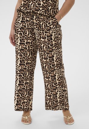 Kobieta ubrana w szerokie spodnie z wysokim stanem w panterkę z kieszeniami, w połączeniu z białymi sandałami ozdobionymi złotym motywem w kształcie muszli.