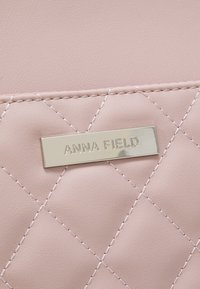 Pochette en similicuir rose avec un motif matelassé en losanges et une étiquette de marque rectangulaire argentée gravée de "ANNA FIELD".