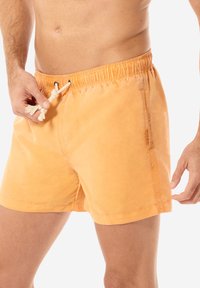 Shorts da nuoto arancioni con cintura elastica, cordoncino e tasca laterale. Realizzati in tessuto leggero con una texture liscia.