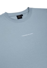 Lichtblauw katoenen t-shirt met een ronde hals. Heeft "TOMORROWLAND" in witte borduursel aan de voorkant. Zachte textuur, casual ontwerp.