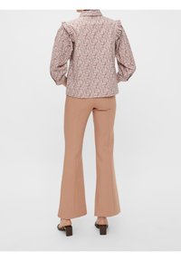Blusa con motivo floreale e maniche a sbuffo, con dettagli arricciati, abbinata a pantaloni beige a zampa d'elefante e sandali con tacco quadrato.