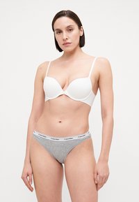 Fehér párnázott melltartó állítható pántokkal és sima textúrával. Szürke tanga fehér Calvin Klein logós derékkal. Egyszerű, klasszikus dizájn.