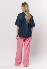 Denim overhemd met korte mouwen en een afgeronde zoom, gecombineerd met roze gestreepte wijde broekspijpen. De outfit heeft een ontspannen pasvorm en een casual ontwerp.