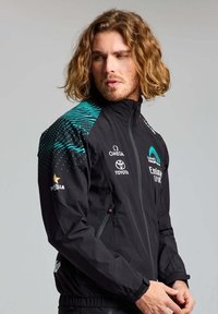 Giacca leggera nera con colletto alto, caratterizzata da un motivo a pois turchese sulle maniche e loghi di sponsor sul davanti e sulla manica.