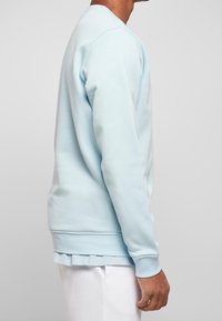 Sweat-shirt bleu clair avec un col rond, des manches longues et des poignets et un ourlet côtelés. Le tissu semble doux avec une texture lisse.