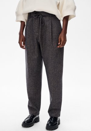 Spodnie z mieszanki wełny w ciemnoszarym kolorze, z elastycznym ściągaczem w pasie, fałdami i zwężanymi nogawkami, połączenie z błyszczącymi czarnymi mokasynami.