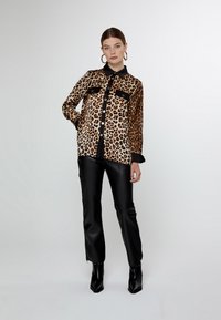 Camicia con stampa leopardata, colletto e bottoni neri, dotata di due tasche sul petto, indossata con pantaloni in ecopelle nera e stivali con tacco.