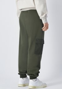 Grüne Cargo-Sweatpants aus weichem Stoff mit übergroßer Passform, gerippten Bündchen und einer Seitentasche mit Druckverschluss.
