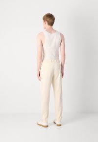 Pantalones ajustados color crema hechos de un tejido suave, con una textura lisa y bolsillos traseros. Se llevan con una camiseta sin mangas blanca y zapatillas blancas.