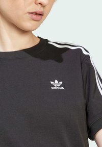 Svart bomull T-skjorte med rund hals, hvit adidas-logo på brystet og hvite side-striper på ermene. Glatt tekstur, standard passform.