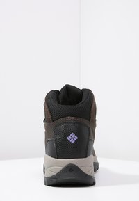 Bota de senderismo marrón y negra con parte superior de malla y cuero, collar acolchado, suela gris y detalle del logo púrpura en el talón.