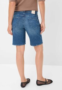 Shorts in denim con un lavaggio blu medio, dal taglio classico, con tasche posteriori e orlo arrotolato. Abbinati a ballerine in rete nere.