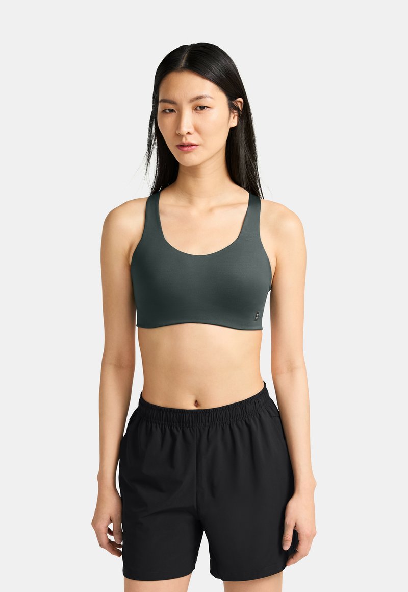 Sujetador deportivo verde oscuro con tirantes anchos y una textura suave, acompañado de pantalones cortos deportivos negros con una cintura elástica.