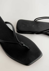Sandales plates noires avec un design à bout carré, dotées de fines lanières et d'un accent noué. Fabriquées en matériau lisse avec un minimum de détails.
