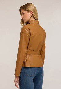 Veste en cuir marron au design ajusté, avec une taille ceinturée et des manches longues. Texture lisse avec un col et des détails de couture subtils.