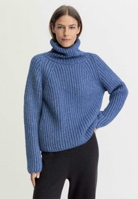 Blauer gestrickter Rollkragenpullover mit grober Textur, Rippmuster und langen Ärmeln. Getragen mit schwarzen Hosen, die eine lockere Passform zeigen.