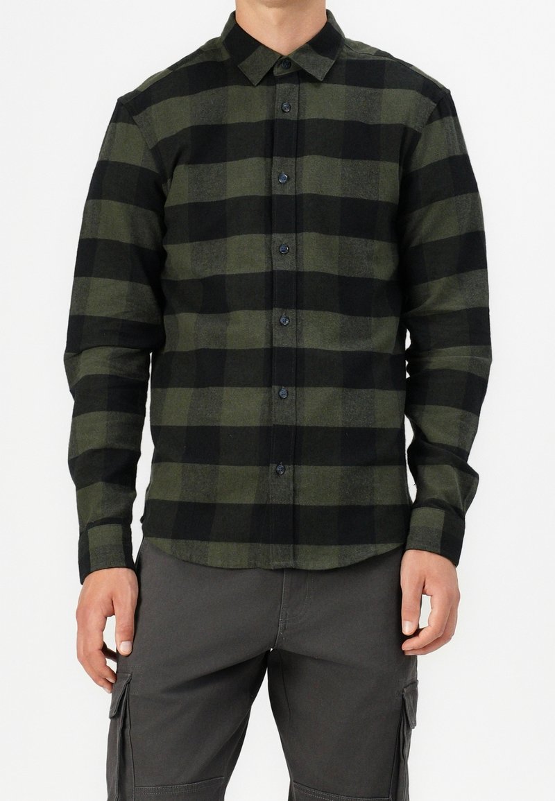 Camicia in flanella a quadri verde e nera con chiusura a bottoni, maniche lunghe e orlo arrotondato. Texture morbida con una leggera lucentezza.