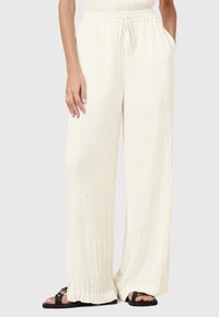 Crème wijde broek van een textuurstof, met een elastische tailleband en een trekkoord, en zijzakken; gecombineerd met zwarte sandalen.