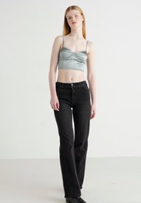 Cropped top in satin verde chiaro con spalline sottili, abbinato a jeans neri a gamba dritta a vita alta, con chiusura frontale a bottoni.