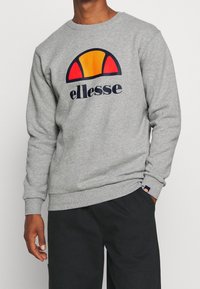 Sweat-shirt gris à manches longues, col rond, grand logo ellesse multicolore, poignets et ourlet côtelés, fabriqué en mélange de coton doux.