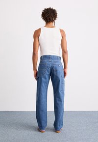 Lys blå denimbukser med rett ben, flere lommer og synlige sømdetaljer. Brukt med en hvit tanktop.