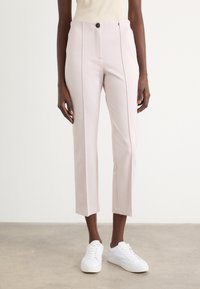 Lichtroze broek met een getailleerd ontwerp, voorzien van een enkele knoopsluiting, voorzakken en een cropped zoom. Gekocht met witte sneakers.