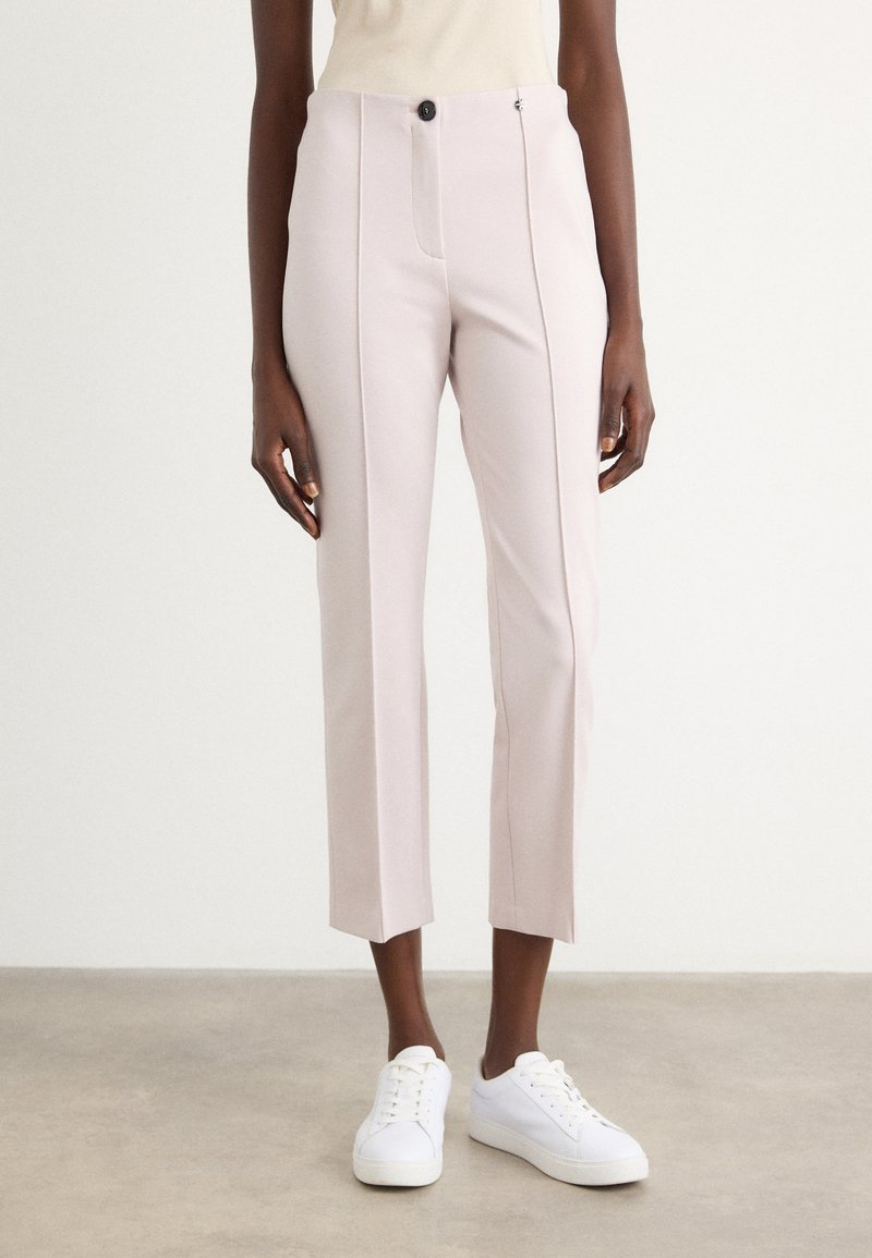 Lichtroze broek met een getailleerd ontwerp, voorzien van een enkele knoopsluiting, voorzakken en een cropped zoom. Gekocht met witte sneakers.