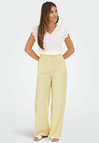 Lichtgele wijde broek met een elastische tailleband en een witte top met kantafwerking op de korte mouwen. Zachte textuur.