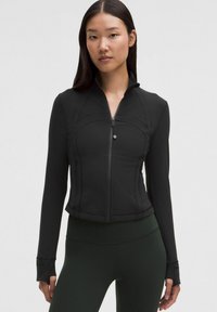 Crna zip-up jakna s uskim krojem, s dugim rukavima, visokim ovratnikom i šavnim detaljima. Nosena s hlačama visokog struka u tamnozelenoj boji.