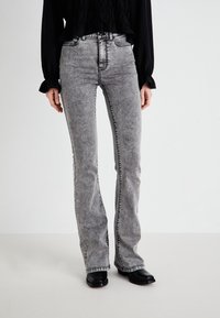 Jean flare gris avec une texture délavée, couture noire contrastante, taille haute et un design classique à cinq poches.