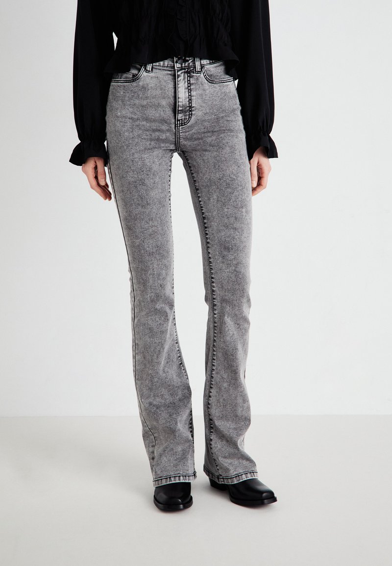 Jean flare gris avec une texture délavée, couture noire contrastante, taille haute et un design classique à cinq poches.
