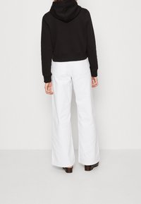 Sudadera negra corta con capucha, combinada con pantalones blancos de pierna ancha y talle alto. El material parece suave y los pantalones tienen costuras mínimas visibles.