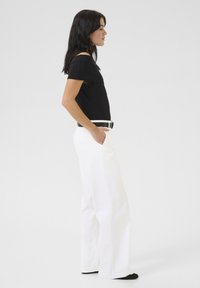 Zwarte top met korte mouwen, gecombineerd met hoge witte wijde broek en een zwarte riem, met een gladde textuur en minimalistisch ontwerp.