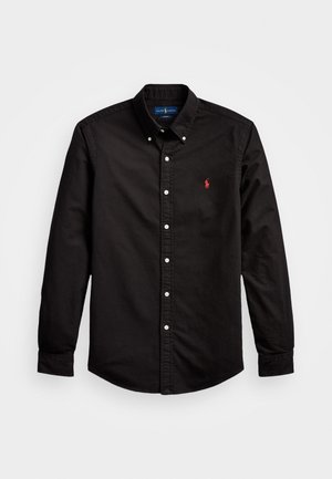 Camisa negra de manga larga con botones y cuello, con un logo bordado en rojo en el lado izquierdo del pecho, extendida sobre un fondo blanco.