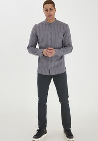 Grå, langermet skjorte med vertikale striper, knappelukking og brystlomme, kombinert med mørke bukser og sorte sneakers.