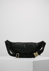 Black faux leather crossbody bag with a curved shape, featuring a textured strap with logo and a gold buckle accent.