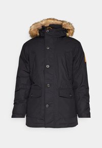 Parka noire isolée avec bordure en fausse fourrure sur capuche, cinq poches frontales et fermeture à boutons. Tissu lisse avec une finition légèrement mate.