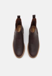 Bottes courtes en cuir marron avec panneaux latéraux élastiques et languettes de tirage. Présentent une texture lisse et une couture de semelle marron clair contrastante.