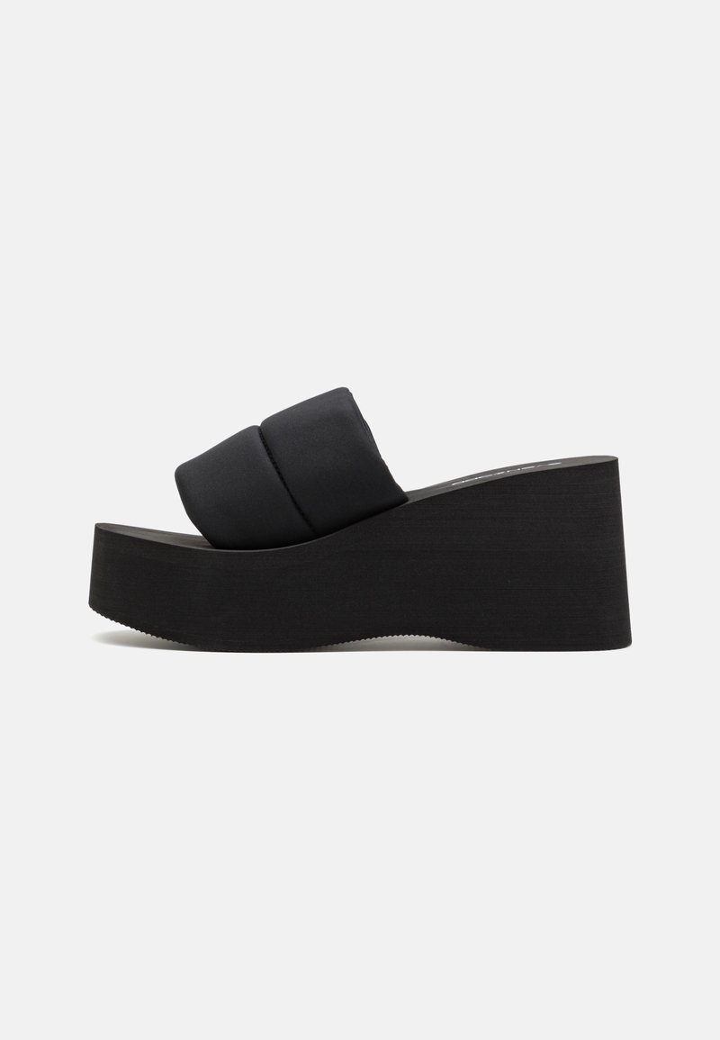 Sandale compensée noire avec une large bride rembourrée épaisse et une semelle texturée, vue de profil sur un fond uni.