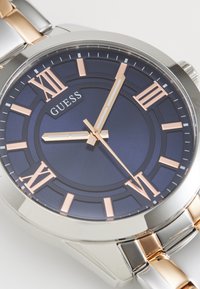 Montre en acier inoxydable argenté et or rose avec un cadran bleu foncé, des chiffres romains et trois aiguilles en or rose. Design de boîtier rond.