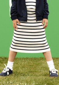 Abito a righe blu navy e bianche con maniche corte, abbinato a sneaker blu navy e calze bianche, su uno sfondo verde.