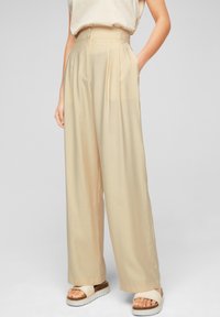 Beige, vida byxor med veck, hög midja och ett slätt, lätt material. Matchas med vita platåsandaler.