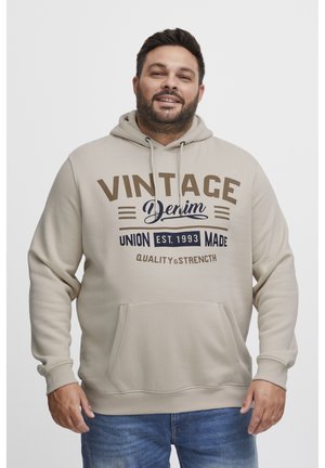 Beige hoodie with a front kangaroo pocket, featuring "VINTAGE Denim" text in dark brown and navy. Drawstring hood and ribbed cuffs.