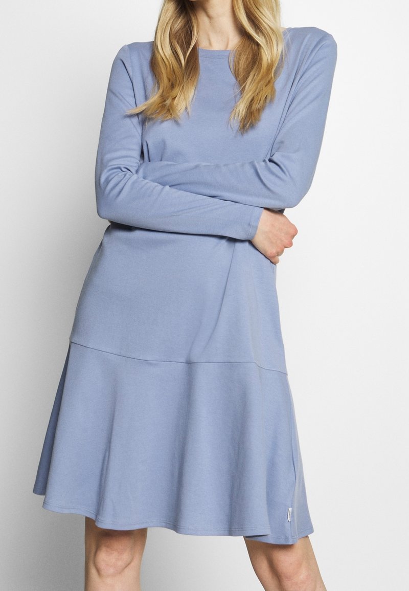 Långärmad, ljusblå klänning med utsvängd kjol. Tillverkad av mjukt tyg, med rundad halsringning och subtil sömdekor.