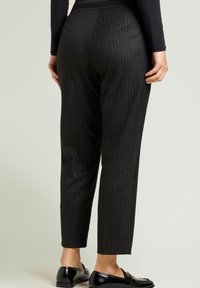 Zwarte pantalon met krijtstreep van gladde stof, met taps toelopende pijpen. Gecombineerd met glanzende zwarte loafers.